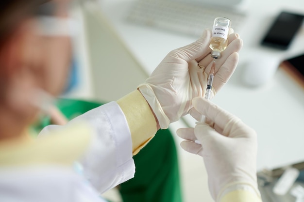 Closeup image of doctor holding syringe and vial with vaccine against coronavirus