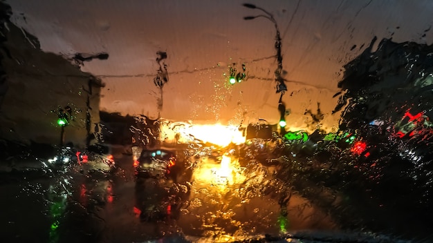 Closeup image of droplets on wet car windshield in rain at sunset light. Abstract shot of wet windscreen an sun rays