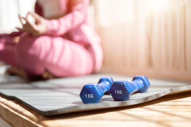 Closeup image of dumbbells on a yoga mat while a woman is meditating