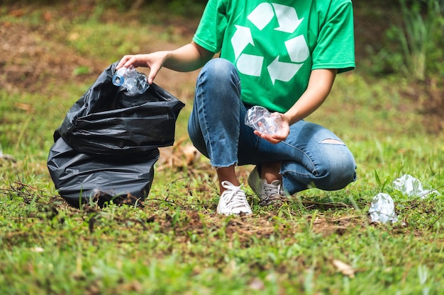 Closeup image of a female activist picking up garbage plastic bottles into a plastic bag in the park for recycling concept