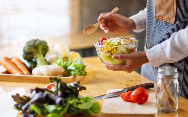 Closeup image of a female chef cooking and holding a bowl of fresh mixed vegetables salad to eat in kitchen