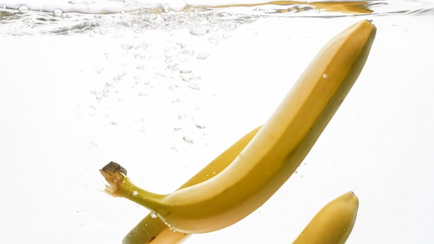 Closeup image of fresh ripe bananas falling and splashing in water