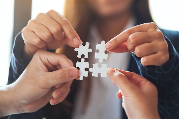 Closeup image of a group of people holding and putting a piece of white jigsaw puzzle together