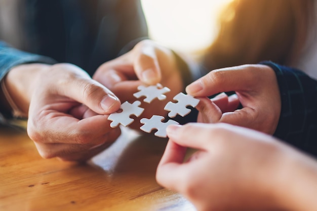 Closeup image of a group of people holding and putting a piece of white jigsaw puzzle together