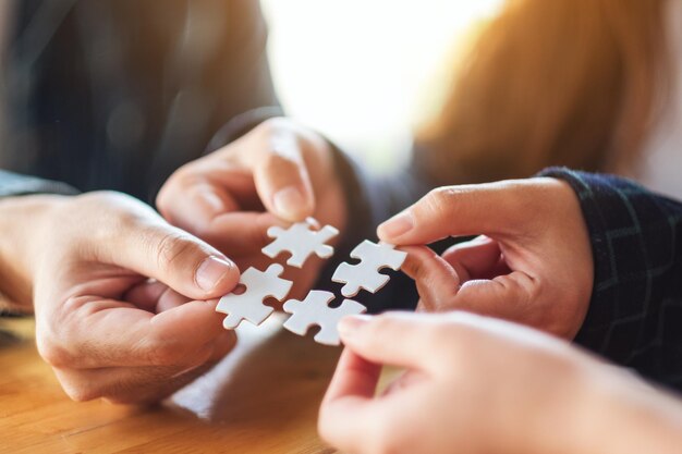 Closeup image of a group of people holding and putting a piece of white jigsaw puzzle together