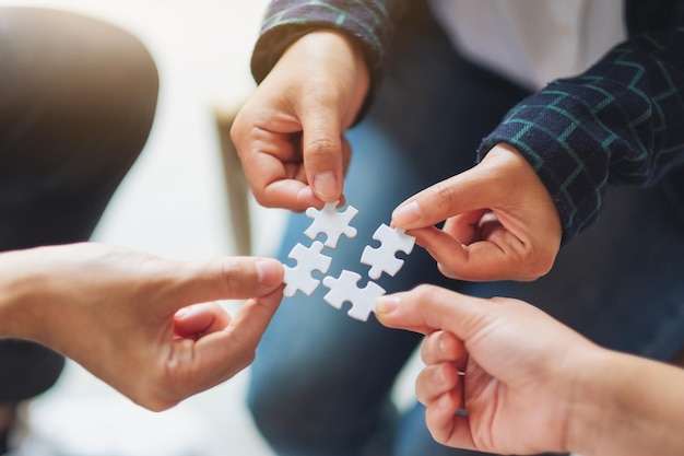 Closeup image of a group of people holding and putting a piece of white jigsaw puzzle together