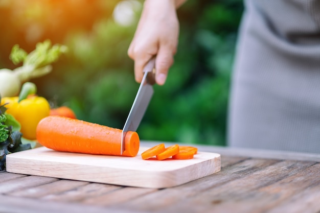 Closeup image of a hand cutting and chopping carrot by knife on wooden board