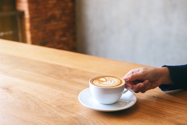 Closeup image of a hand holding a cup of hot coffee on wooden table