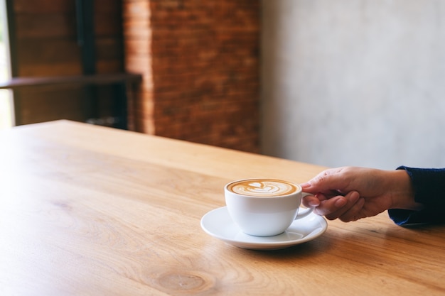 Closeup image of a hand holding a cup of hot coffee on wooden table