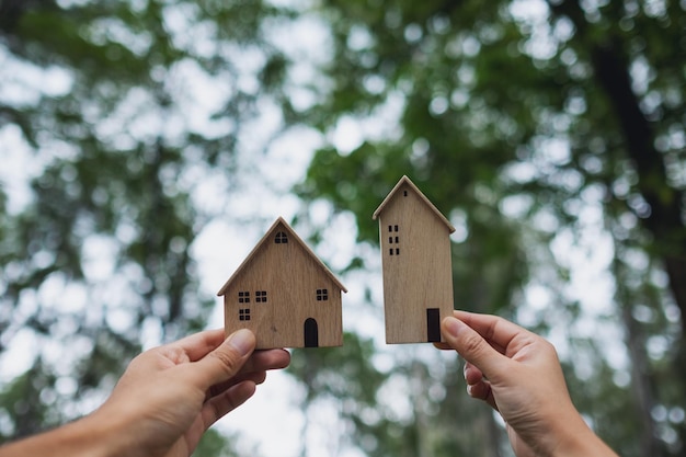 Closeup image of hands holding and showing wooden house models with nature background