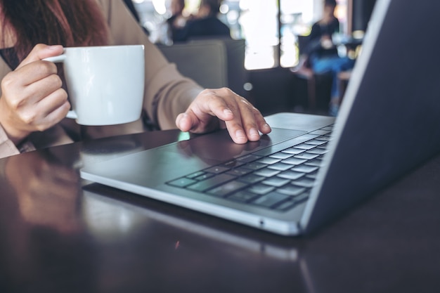 Closeup image of hands using and touching on laptop touchpad while drinking coffee in cafe