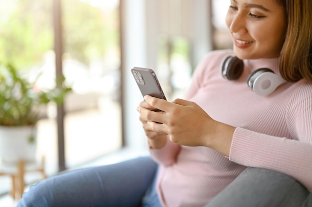 Closeup image of a happy Asian woman using her smartphone while relaxing in living room