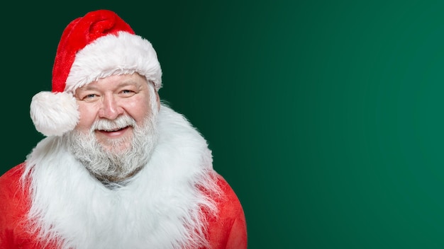 Closeup image of a happy Santa Claus dressed in a red coat and a hat, isolated green background. Space for text.