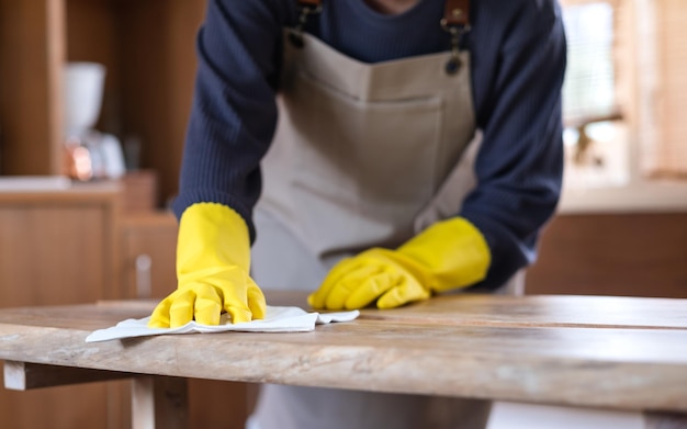 Closeup image of a housewife wearing protective glove cleaning and washing wooden table at home