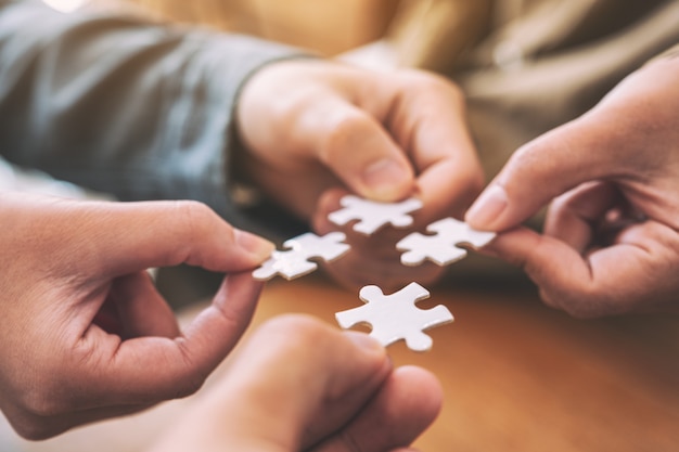 Closeup image of many people hands holding and putting a piece of white jigsaw puzzle together