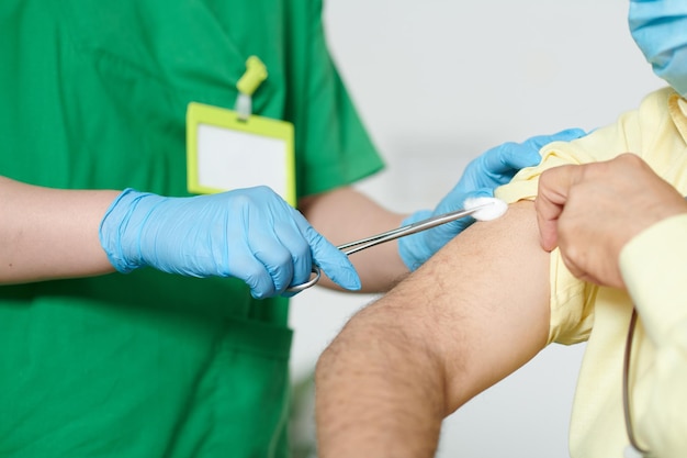 Closeup image of nurse in rubber gloves wiping shoulder of patient with cotton ball before injecting vaccine