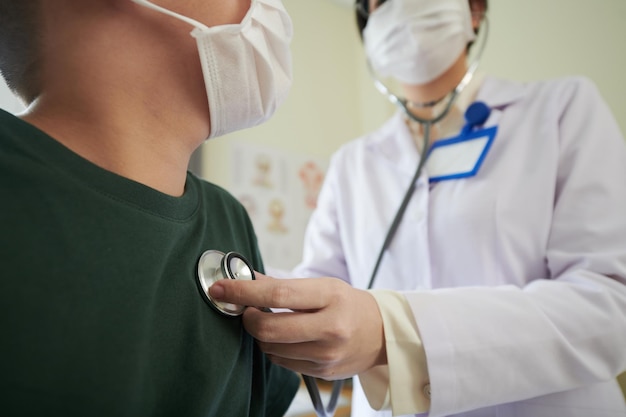 Closeup image of pediatrician with stethoscope checking heartbeat of little patient in medical mask