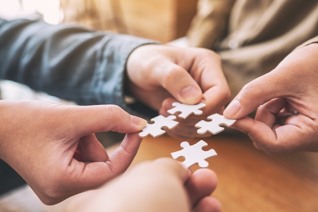 Closeup image of people's hands holding and putting a piece of white jigsaw puzzle together