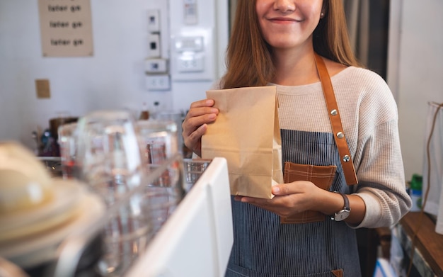 Closeup image of a waitress holding and serving a takeaway food in paper bag to customer in a shop