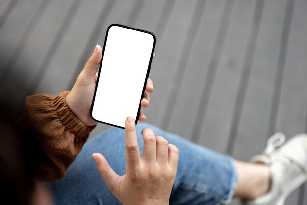 Closeup image of a woman in casual clothes sitting outdoors in the city and using her smartphone