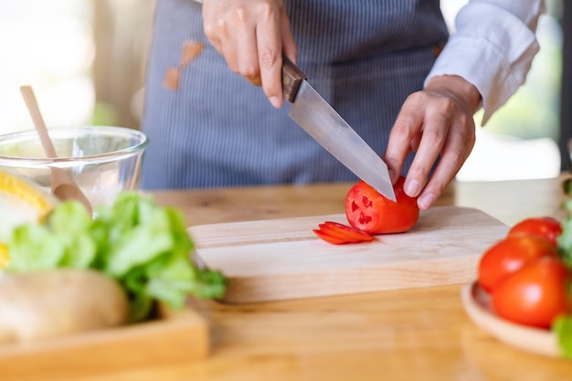 Closeup image of a woman chef cutting and chopping tomato by knife on wooden board