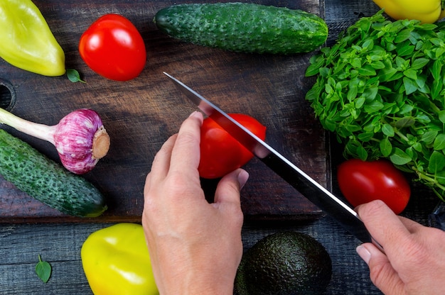 Closeup image of a woman cutting and chopping tomato by knife on wooden board