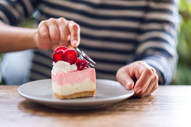 Closeup image of a woman eating a strawberry cheese cake in a plate