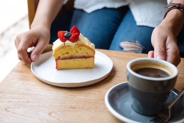 Closeup image of a woman holding a cake and coffee cup in cafe