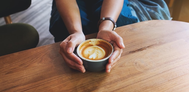 Closeup image of a woman holding a cup of coffee with latte art