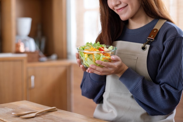 Closeup image of a woman holding a fresh mixed vegetables salad in the kitchen at home