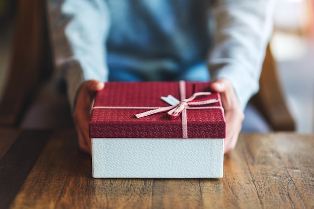 Closeup image of a woman holding and giving a red gift box