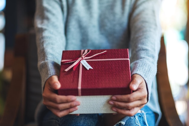 Closeup image of a woman holding and giving a red gift box