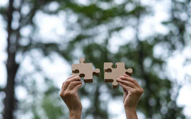 Closeup image of a woman holding and putting a piece of wooden jigsaw puzzle together in the outdoors