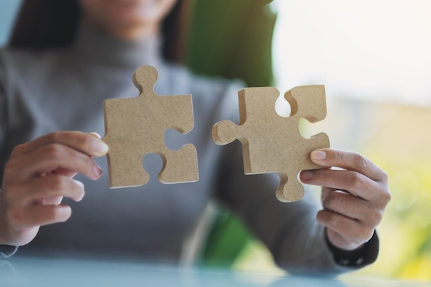 Closeup image of a woman holding and putting a piece of wooden jigsaw puzzle together