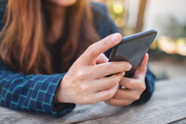 Closeup image of a woman holding , using and looking at mobile phone in the outdoors