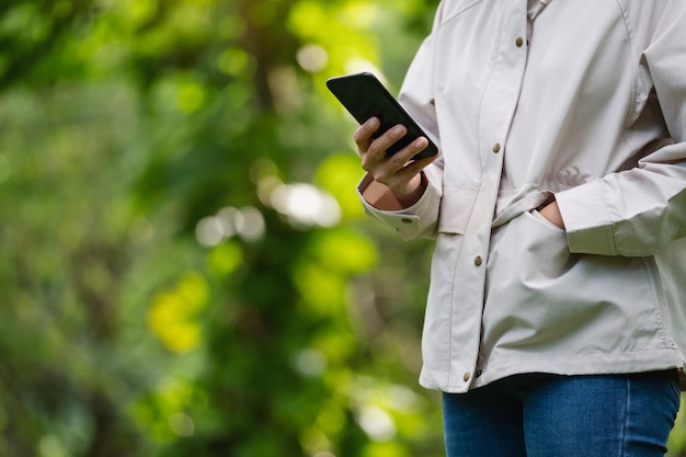 Closeup image of a woman holding and using mobile phone in the outdoors