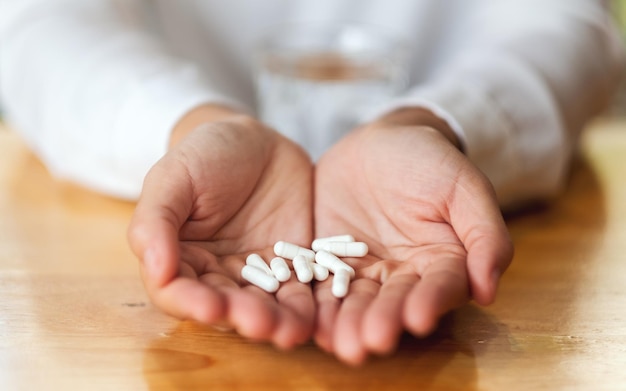 Closeup image of a woman holding white medicine capsules in hands