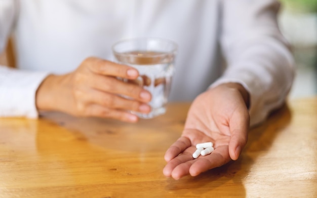 Closeup image of a woman holding white pills and a glass of water