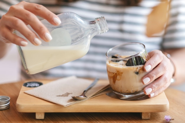 Closeup image of a woman pouring milk into a glass of ice cube coffee in cafe