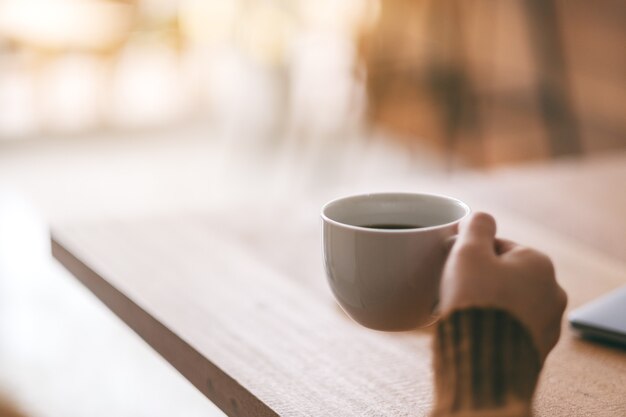 Closeup image of a woman's hand holding a white cup of hot coffee to drink