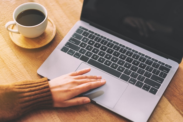 Closeup image of a woman's hand using and touching on laptop touchpad on wooden table