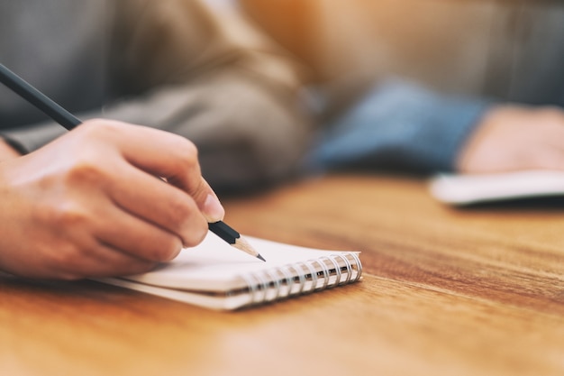 Closeup image of a woman's hand writing on blank notebook on wooden table