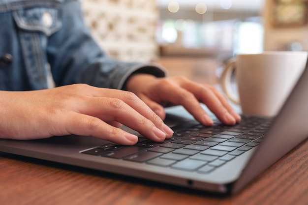 Closeup image of woman's hands using and typing on laptop computer keyboard with coffee cup on the table