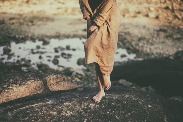 Closeup image of a woman's legs while  standing on the rock by the beach