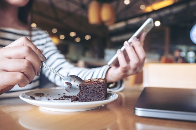 Photo closeup image of a woman using smartphone while eating cake