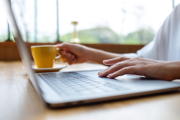 Closeup image of a woman working and touching on laptop computer touchpad while drinking coffee