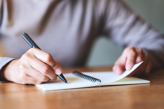 Closeup image of a woman writing on a blank notebook on the table