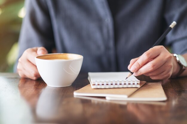 Closeup image of a woman writing on blank notebook while drinking coffee