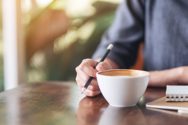 Closeup image of a woman writing on blank notebook while drinking coffee