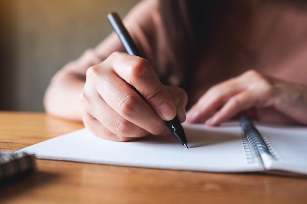 Closeup image of a woman writing on a blank notebook on wooden table